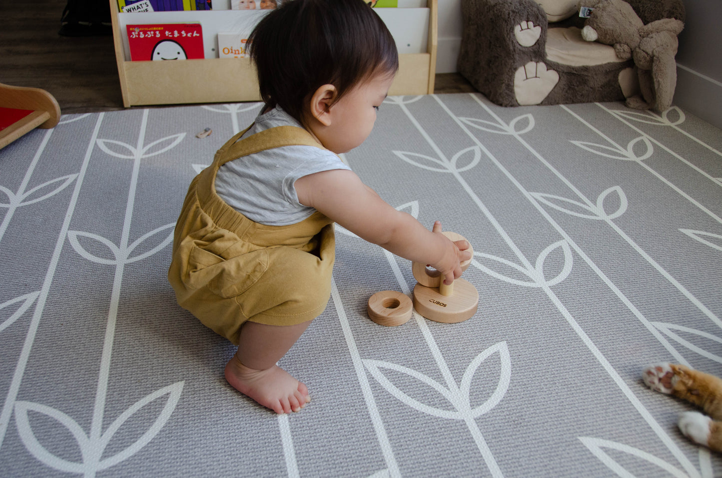 Sweet baby girl eagerly attempting to put the first ring on the Vertical Dowel, showing determination and perseverance as she practices her hand-eye coordination and problem-solving skills during her playful exploration.