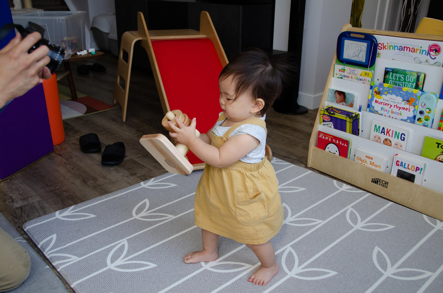 Brilliant baby girl successfully stacks all three wooden rings on the Cubos Horizontal Dowel Rings Stacker, beaming with joy and excitement at her accomplishment. She proudly picks up the whole toy and hurries to show her creation to her proud and delighted parents, who cheer her on for her fantastic playtime achievement.