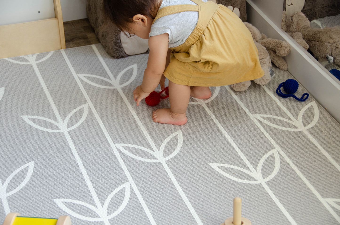 Sweet baby girl carefully picking up red yarn balls, her tiny hands reaching for the soft textures, captivated by the playful exploration during her endearing playtime.