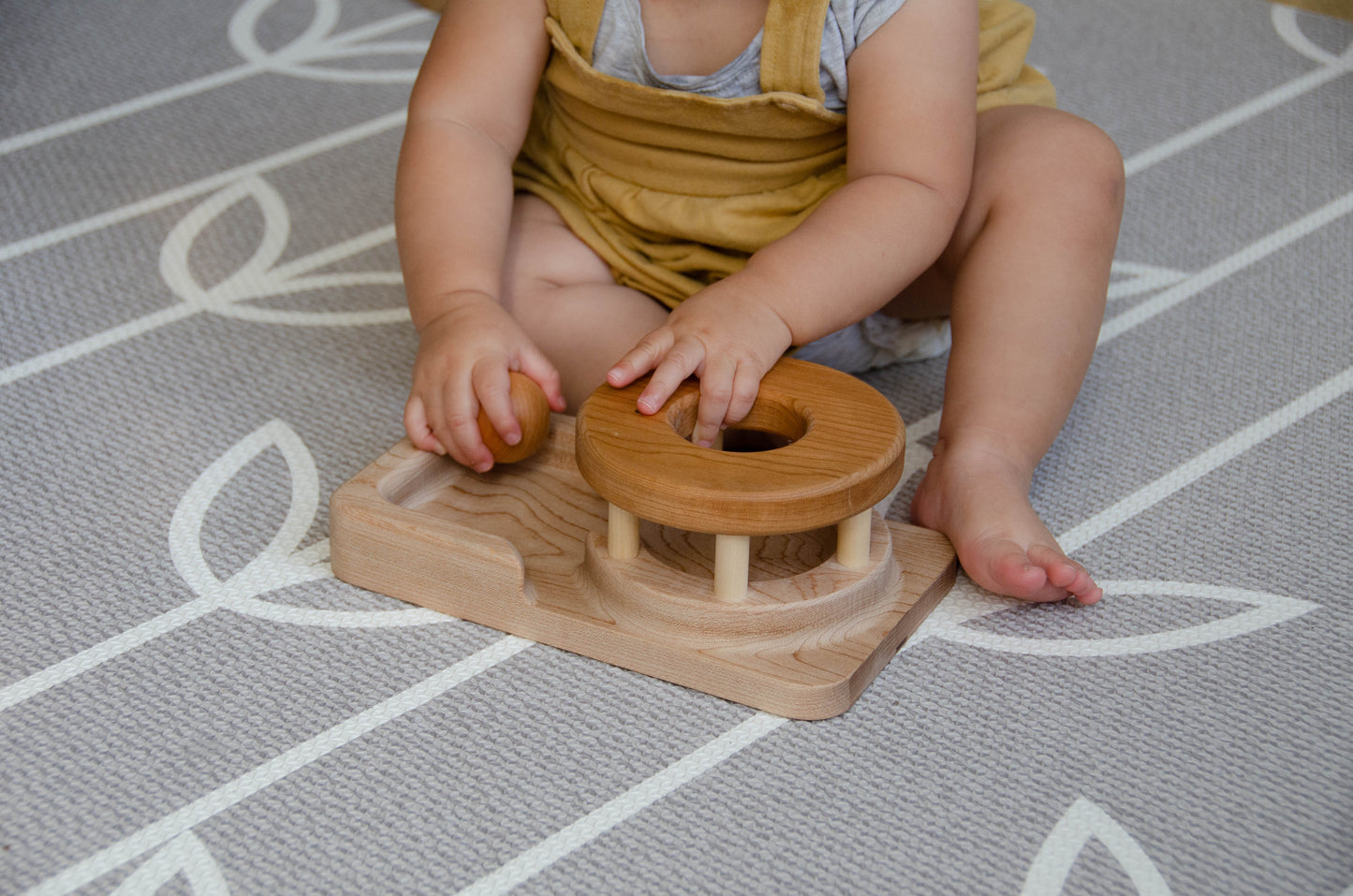 The baby girl is engrossed in play with the Permanence Box, a classic Montessori toy. With great curiosity and excitement, she explores the various compartments, practicing her hand-eye coordination and fine motor skills as she discovers the joy of fitting objects into their designated spaces. This educational and interactive playtime experience helps her develop an understanding of object permanence and spatial relationships, providing a foundation for her cognitive development.