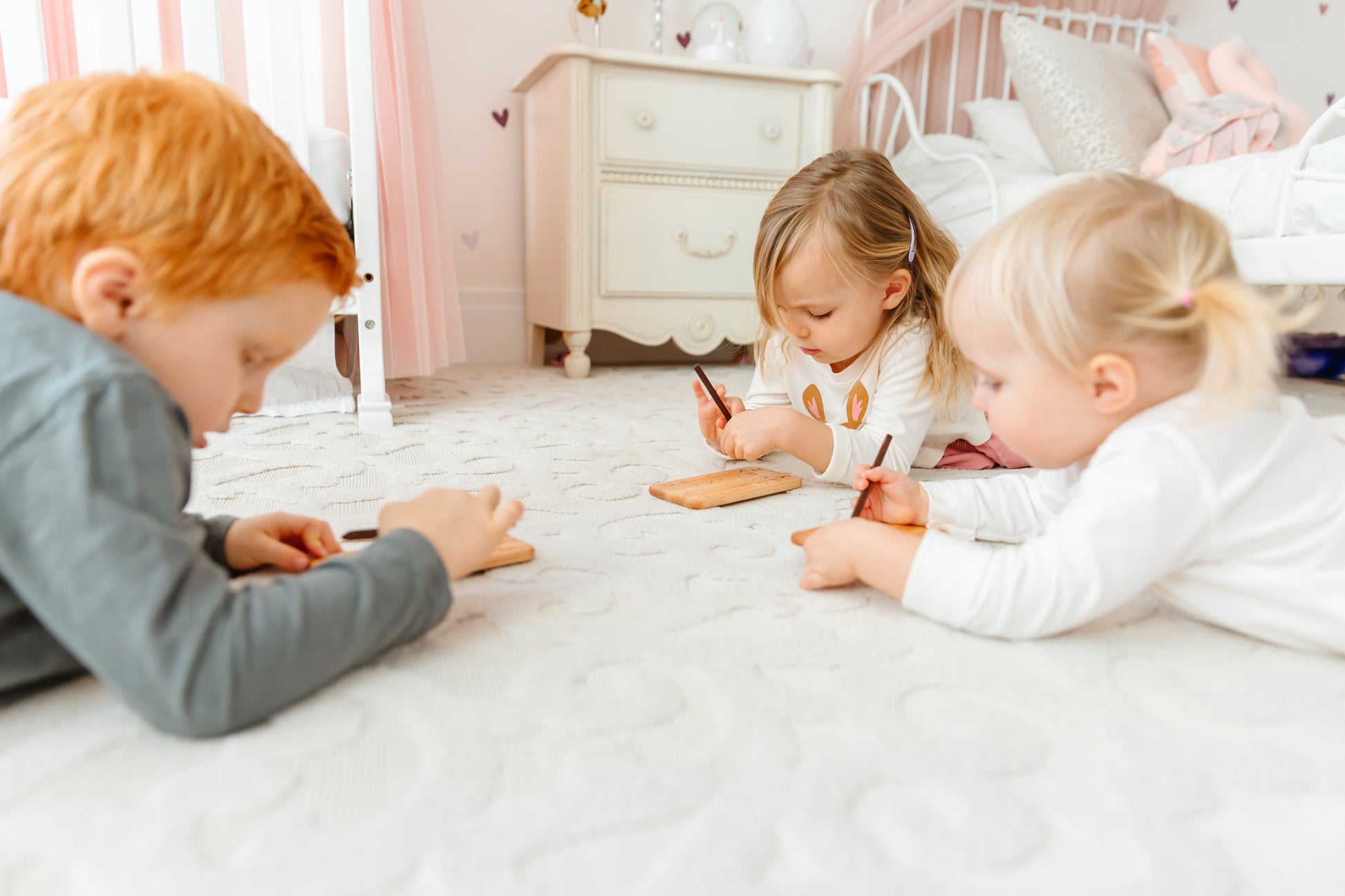 Three little kids lying on the floor, engrossed in play, using iDoddle to trace and write both the alphabet and numbers. Their playful engagement with the wooden toy fosters learning and creativity as they explore letters, numbers, and colors, all while enjoying the camaraderie of shared playtime. This interactive activity not only enhances their cognitive development but also strengthens their friendship and social skills.