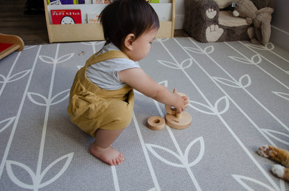 Sweet baby girl eagerly attempting to put the first ring on the Vertical Dowel, showing determination and perseverance as she practices her hand-eye coordination and problem-solving skills during her playful exploration.