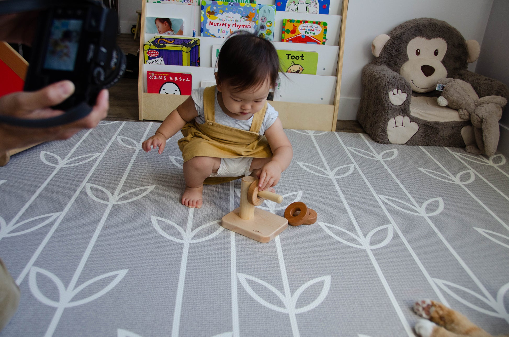 Adorable baby girl excitedly placing the first wooden ring on the Cubos Horizontal Dowel Rings Stacker, beginning her delightful journey of exploration and learning with the engaging wooden toy.