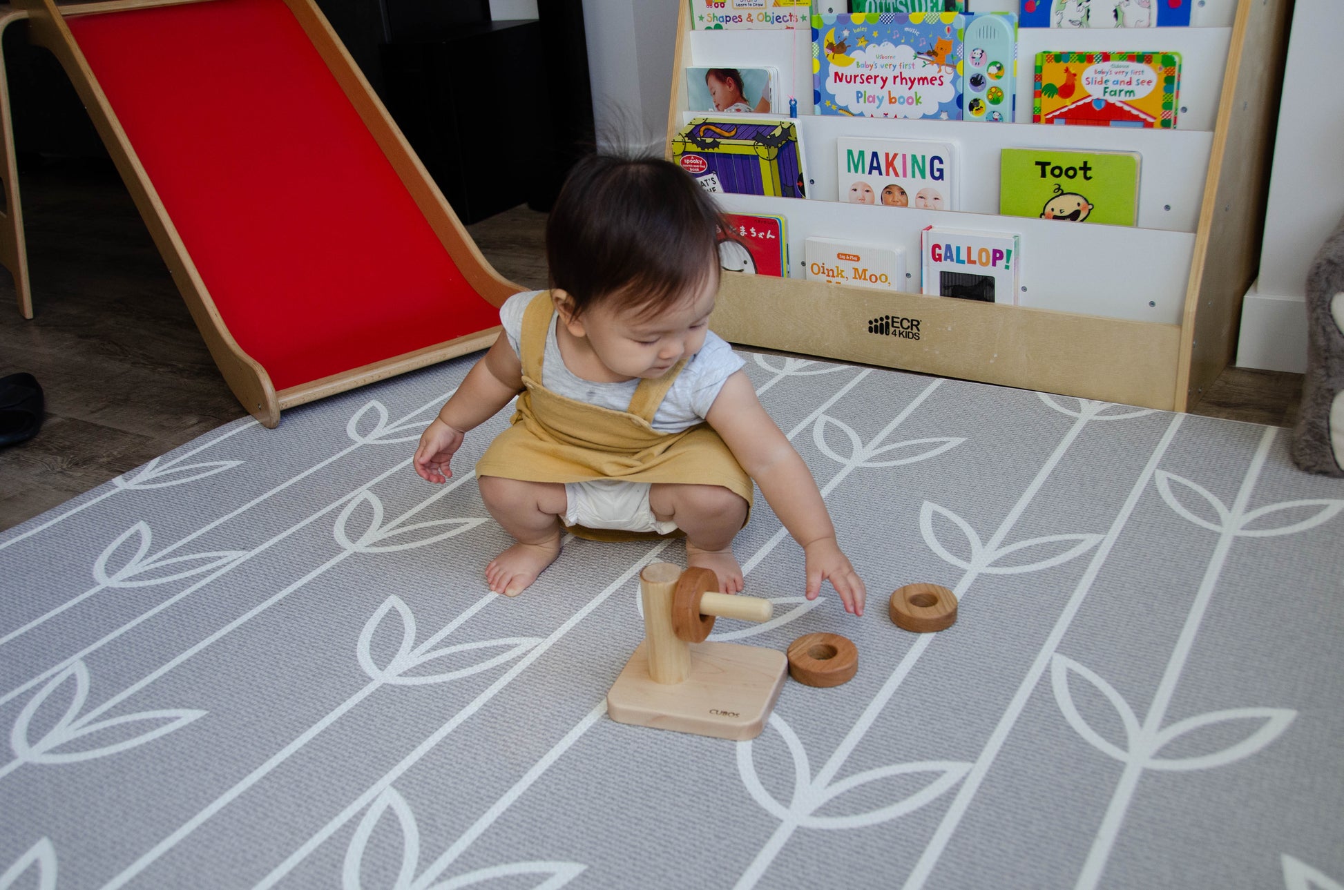 Endearing baby girl eagerly reaching out to grasp the second wooden ring for the Cubos Horizontal Dowel Rings Stacker, demonstrating her determination and developing fine motor skills as she continues her captivating playtime activity.