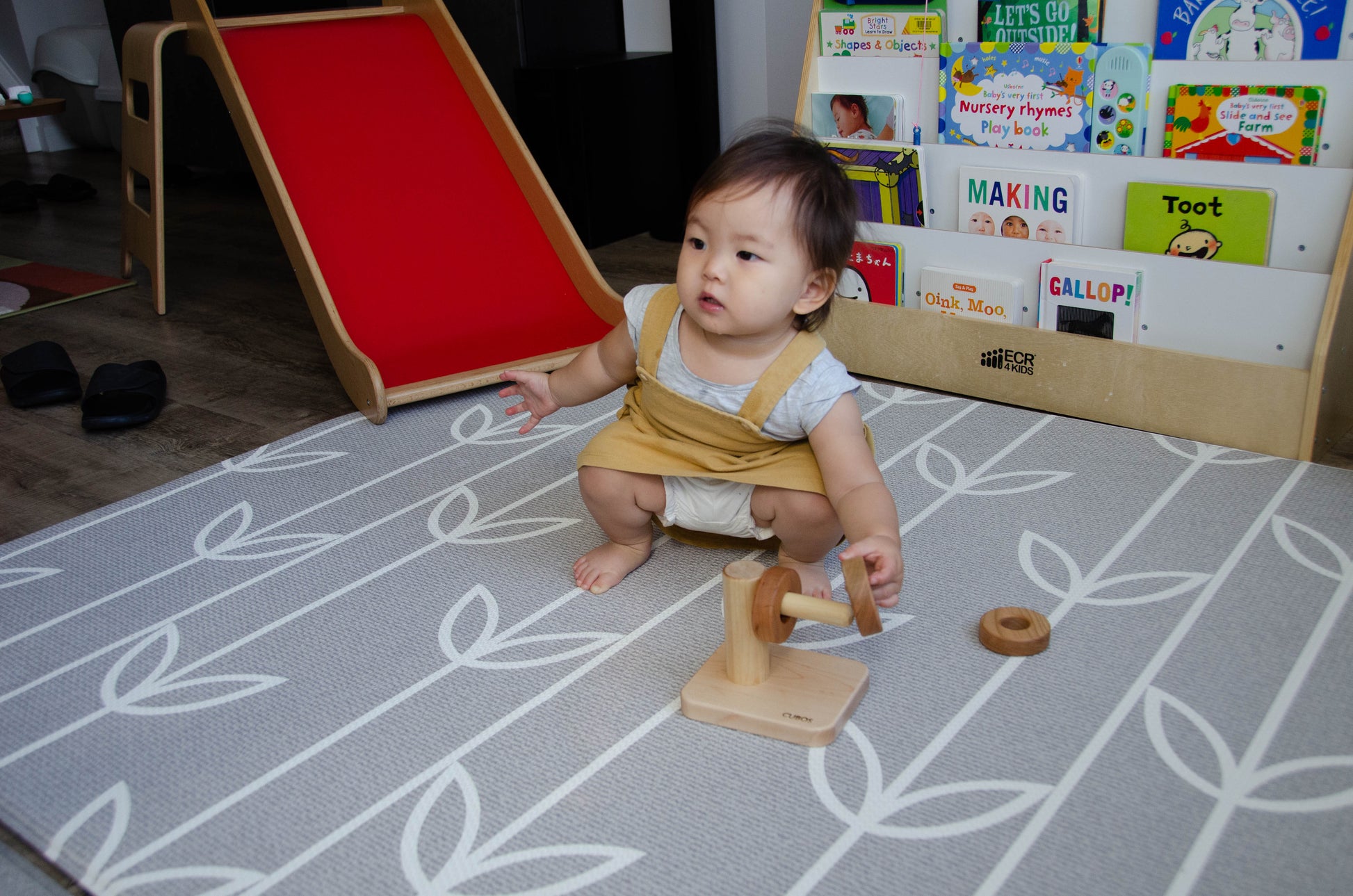 Sweet baby girl successfully putting the second wooden ring on the Cubos Horizontal Dowel Rings Stacker, celebrating her progress and growing confidence in stacking the rings with each accomplishment. Her playful exploration and motor skills development continue to shine during this delightful playtime.