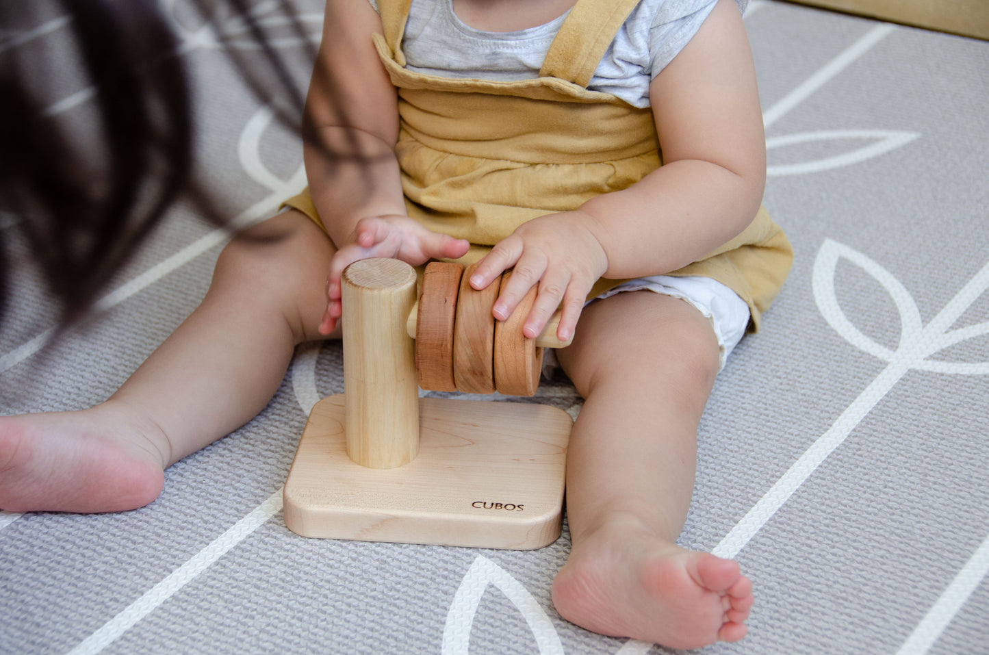 Brilliant baby girl successfully stacking all three wooden rings on the Cubos Horizontal Dowel Rings Stacker, showcasing her achievement and developing her problem-solving skills with each successful placement.