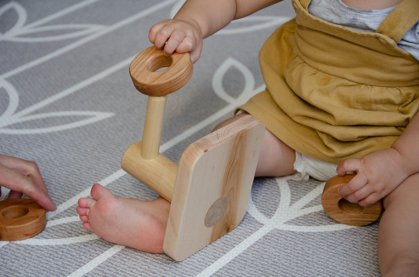 Baby girl happily engaged with the natural wooden Horizontal Dowel Rings Stacker, enjoying the tactile experience as she explores the rings and practices her coordination skills during playtime.