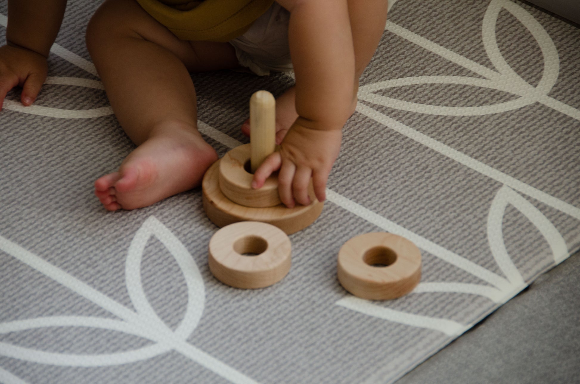 In a heartwarming close-up, the baby girl's tiny hands gently place the first ring on the Vertical Dowel. With focused determination and a sense of accomplishment, she navigates the task, showcasing her early motor skills and concentration during this precious playtime moment.