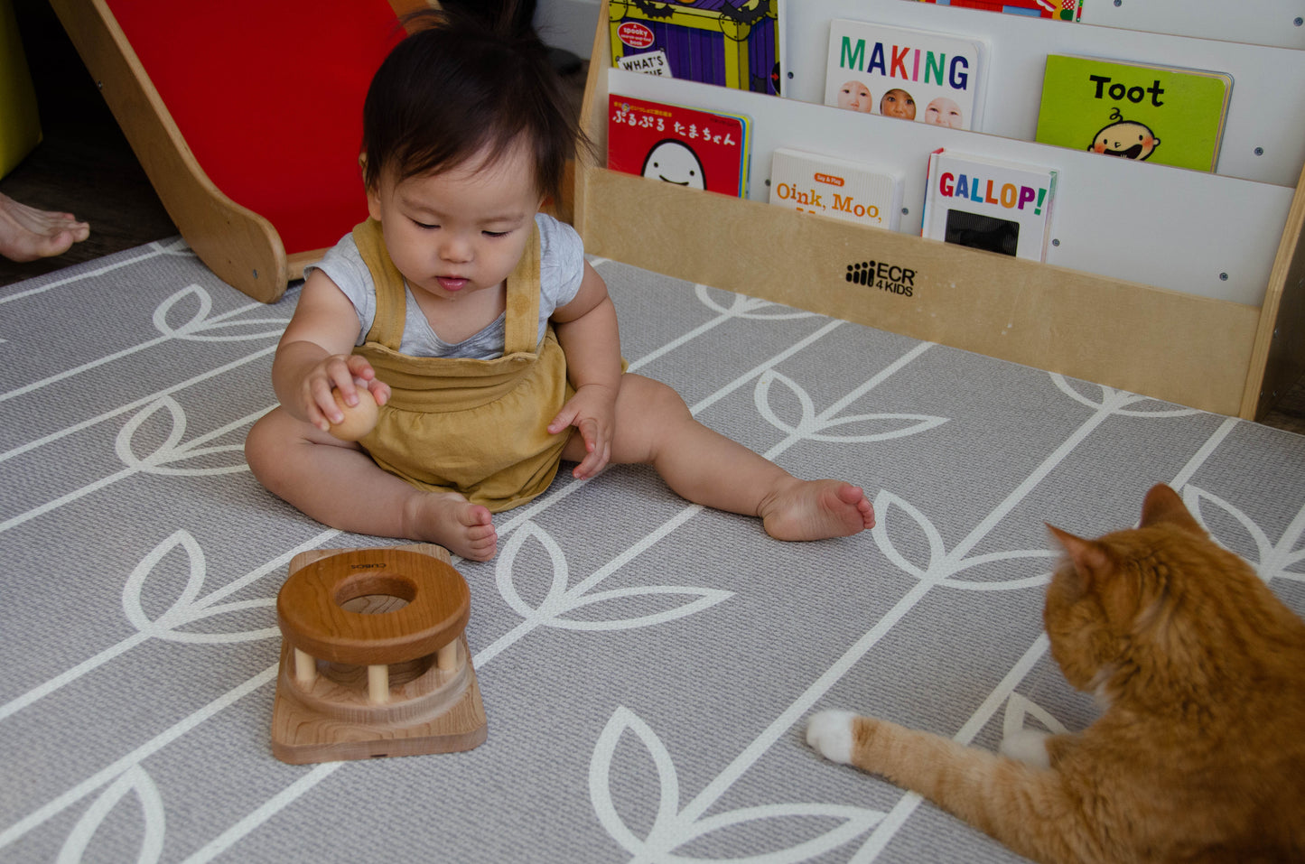 The baby girl is engrossed in play with the Permanence Box, a classic Montessori toy. With great curiosity and excitement, she explores the various compartments, practicing her hand-eye coordination and fine motor skills as she discovers the joy of fitting objects into their designated spaces. This educational and interactive playtime experience helps her develop an understanding of object permanence and spatial relationships, providing a foundation for her cognitive development.