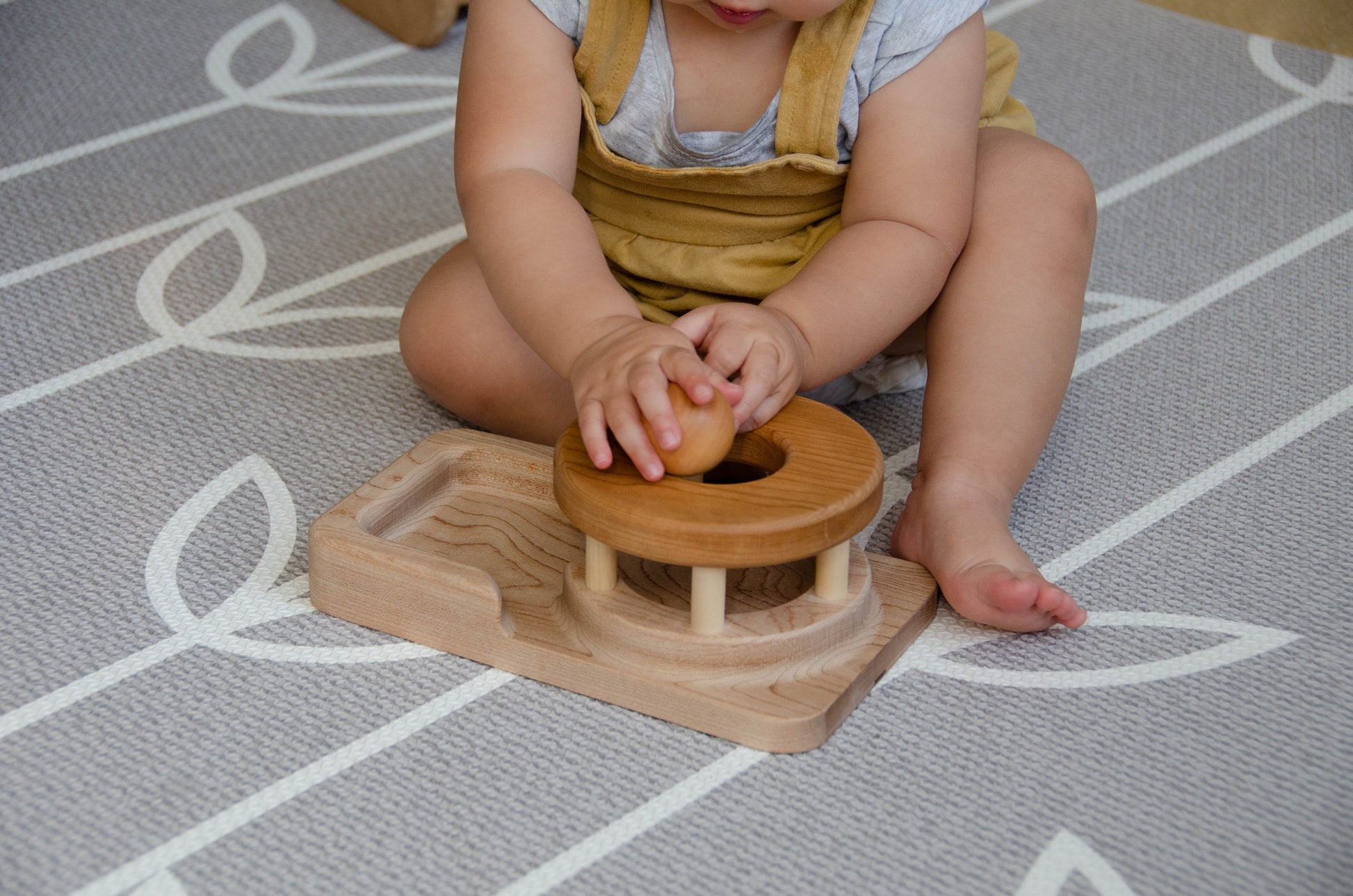 The baby girl is engrossed in play with the Permanence Box, a classic Montessori toy. With great curiosity and excitement, she explores the various compartments, practicing her hand-eye coordination and fine motor skills as she discovers the joy of fitting objects into their designated spaces. This educational and interactive playtime experience helps her develop an understanding of object permanence and spatial relationships, providing a foundation for her cognitive development.