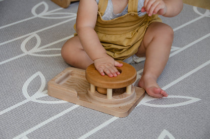 The baby girl is engrossed in play with the Permanence Box, a classic Montessori toy. With great curiosity and excitement, she explores the various compartments, practicing her hand-eye coordination and fine motor skills as she discovers the joy of fitting objects into their designated spaces. This educational and interactive playtime experience helps her develop an understanding of object permanence and spatial relationships, providing a foundation for her cognitive development.