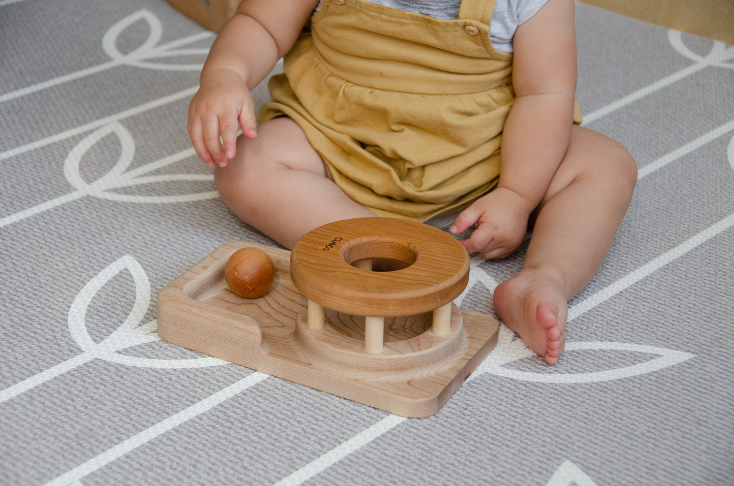 The baby girl is engrossed in play with the Permanence Box, a classic Montessori toy. With great curiosity and excitement, she explores the various compartments, practicing her hand-eye coordination and fine motor skills as she discovers the joy of fitting objects into their designated spaces. This educational and interactive playtime experience helps her develop an understanding of object permanence and spatial relationships, providing a foundation for her cognitive development.