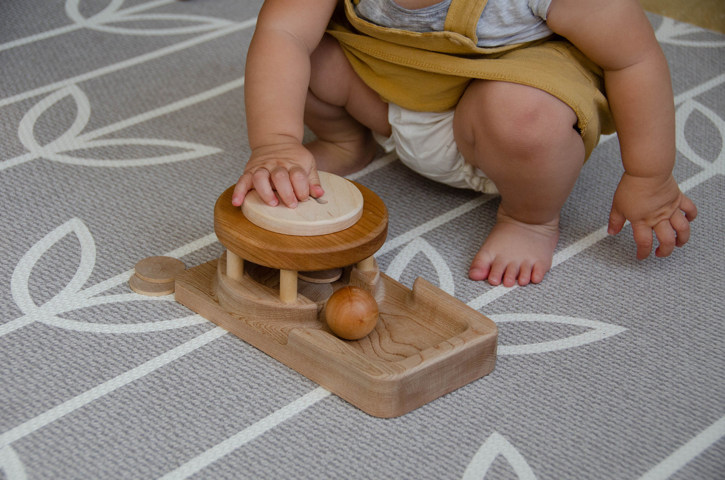 The baby girl is engrossed in play with the Permanence Box, a classic Montessori toy. With great curiosity and excitement, she explores the various compartments, practicing her hand-eye coordination and fine motor skills as she discovers the joy of fitting objects into their designated spaces. This educational and interactive playtime experience helps her develop an understanding of object permanence and spatial relationships, providing a foundation for her cognitive development.