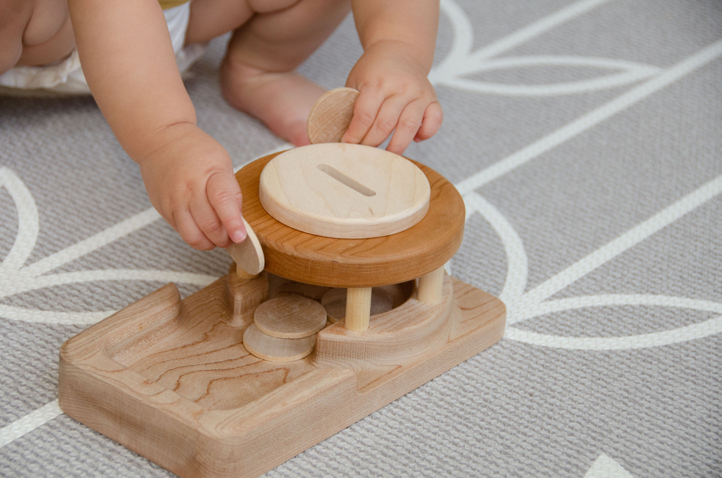 The baby girl is engrossed in play with the Permanence Box, a classic Montessori toy. With great curiosity and excitement, she explores the various compartments, practicing her hand-eye coordination and fine motor skills as she discovers the joy of fitting objects into their designated spaces. This educational and interactive playtime experience helps her develop an understanding of object permanence and spatial relationships, providing a foundation for her cognitive development.