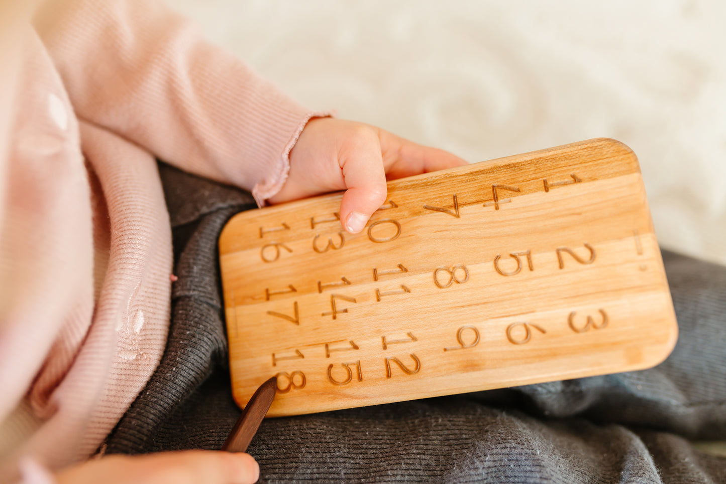 Little baby boy joyfully playing with iDoddle, using it to trace and practice writing numbers from 1 to 18. This interactive and educational activity helps him develop his counting skills and fine motor abilities while having fun with the wooden toy.