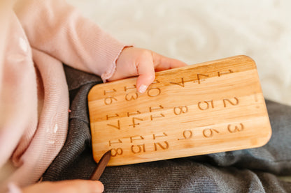 Little baby boy joyfully playing with iDoddle, using it to trace and practice writing numbers from 1 to 18. This interactive and educational activity helps him develop his counting skills and fine motor abilities while having fun with the wooden toy.